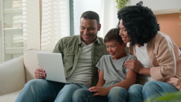 多种族父母夫妇和小儿子坐在沙发上看有趣的电影卡通片快乐的妈妈爸爸在家里教孩子用家庭互联网和现代笔记本电脑 — 图库视频影像