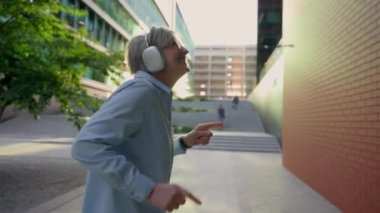 Açık havada dans eden Kafkasyalı iş kadını neşeli neşeli neşeli neşeli neşeli neşeli neşeli neşeli orta yaşlı yaşlı kadın iş kadını kulaklıkla müzik dinliyor kadın ofis müdürü şehrin zafer dansında dans etmeyi seviyor