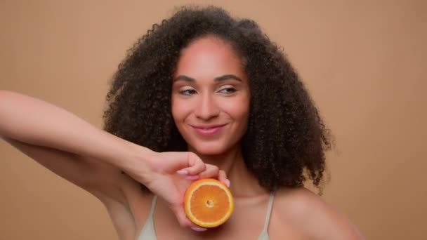 米色背景的肖像为非洲裔美国女孩做广告 非洲裔美国女性拥有一半桔子柑橘类维生素抚慰眨眼健康皮肤护发卷发水果天然有机化妆品 — 图库视频影像