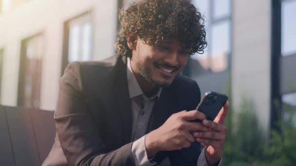 笑顔でスマートフォンを使用してハッピー笑顔のインドのビジネスマン スマートフォンで良いニュースを読むアラビアの男ビジネス雇用者 イスラム教徒男性 起業家 携帯電話をチャット — ストック動画