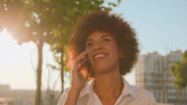 笑顔のアフリカ系アメリカ人幸せなエスニックガールのビジネスウーマン 太陽の光の街を歩くリモートトーク 携帯電話の笑顔の終わり ビジネスコール 女性雇用主 女性は屋外に出る — ストック動画