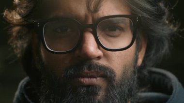 Aşırı derecede yakın, gözlüklü ciddi bir Arap erkek yüzü. Fotoğraf makinesindeki fotoğrafa bakıyor. Müslüman, sakallı, Hintli.