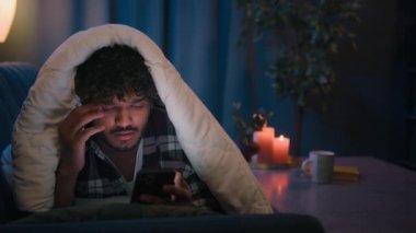 Evde İspanyol adam zımbırtısı internet sosyal medya müptelası sosyal medyada haber okumaktan yorgun, uykulu adam şaşkın, kafası karışmış, kafası karışmış, cep telefonu uygulaması ile yorulmuş Hintli bir erkek.