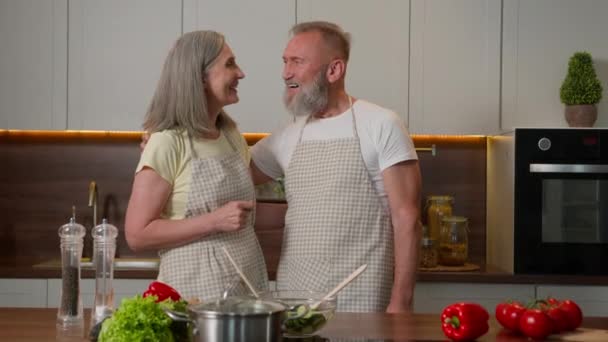 白种人家庭画像快乐的老夫妇退休的妇女祖母和男人爷爷一起做饭健康的食物中年房主的妻子和丈夫欢迎在家里厨房做手势邀请 — 图库视频影像
