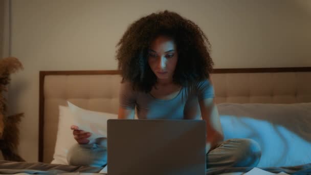 非洲裔美国女商人在家工作文书工作笔记本电脑加班深夜加班检查家用电器账单女学生准备考试晚上在床上学习 — 图库视频影像