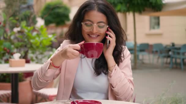 ハッピー笑顔のインドのアラビアの民族女性少女訪問者カフェの朝にカップコーヒーを飲む女性ビジネスマン話す携帯電話ビジネス フレンドリーな話 スマートフォン 話し合いのニュース — ストック動画
