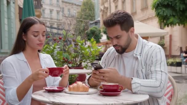 コーカサス カップル 朝食を食べる 街のカフェ 屋外で 忙しい男 携帯電話を使用して ガールフレンド 怒った腕 クロス — ストック動画