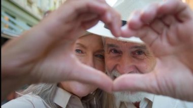 Kapalı portre mutlu beyaz erkek yaşlı aile çift kameraya birleşmiş parmaklarıyla bakıyor aşk jestleri, açık havada romantik sevgililer gününü kutluyor.