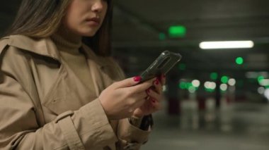 Ciddi Asyalı Çinli Çinli kadın etnik Japon kadın iş kadını müşteri araba parkında cep telefonu siparişi taksisi kullanıyor ve yeraltındaki akıllı telefonlardan mesaj gönderiyor.