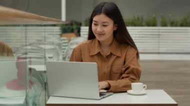 Asyalı güzel Çinli iş kadını dizüstü bilgisayarla çalışıyor kahve içiyor Koreli Japon iş kadını bilgisayar sohbetinde yazı yazıyor ve kafede kablosuz internet kullanıyor.
