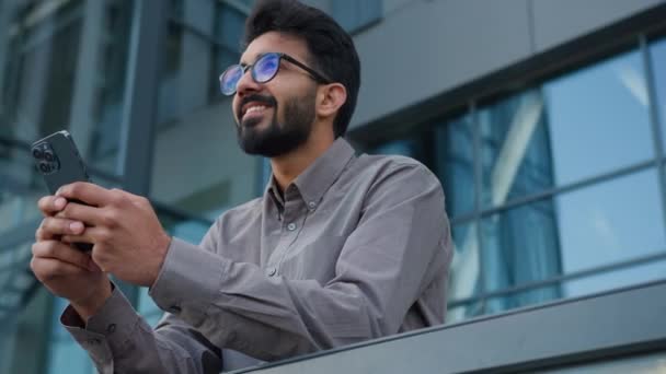 インドのアラビア人男性起業家ワーカースマートビジネスマンオフィスマネージャーは スマートフォンをブラウジングするビジネスアイデアの洞察ジェスチャーメッセージを作成するオンラインチャットの外に携帯電話を保持します — ストック動画