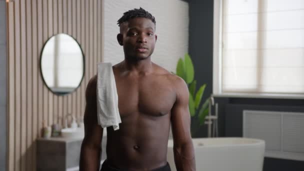 非裔美国人男子微笑着 拿着浴巾看着相机 露出大拇指姿势快乐地赤身裸体运动员早上淋浴卫生习惯在浴室里宣传护肤美容美发 — 图库视频影像