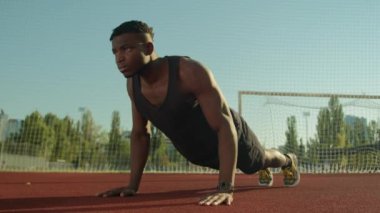 Atletik vücut geliştirici Afrikalı Amerikalı sporcu genç adam futbol stadyumunda şınav çekiyor erkek atlet fitness kasları çalıştırıyor açık hava sporları ve motivasyon.