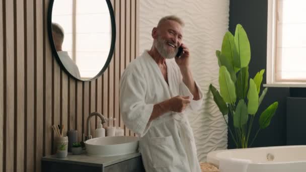 快乐面带微笑的白种人退休老人与智能手机通友好电话打长途电话打长途电话年长的60多岁男子在浴室里洗澡讲手机早间卫生 — 图库视频影像
