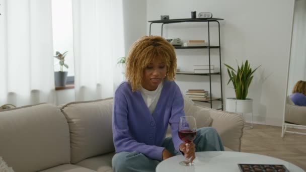 ハッピーケアフリーリラックスアフリカ系アメリカ人の女の子 リラックスして仕事の翌日ホームソファでドリンクを楽しむ アルコール飲料 笑顔の女性 リビングルームで女性 赤ワイン悪い習慣のガラスを保持 — ストック動画