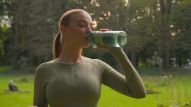 Kafkas formundaki zayıf kadın fitness kızı sportmen kadın spor şişesinden su içiyor taze su iyi sağlık yeşil elma vitaminleri spor vitaminleri spor beslenmesi kilo kaybı parkta açık havada sağlıklı yaşam tarzı