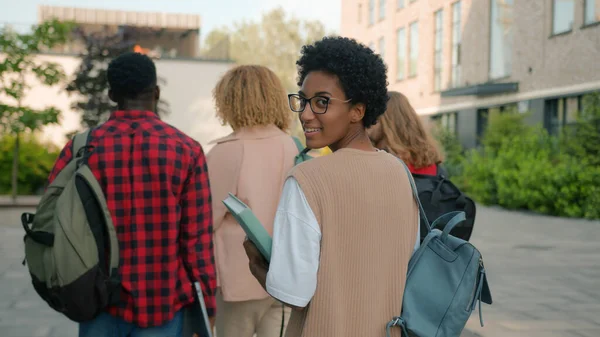Çeşitli üniversite arkadaşları lise öğrencileri, çok kültürlü sınıf arkadaşları dışarıda yürüyüş yapmak için acele eden Afrikalı Amerikalı öğrenci kameraya gülümsüyor.