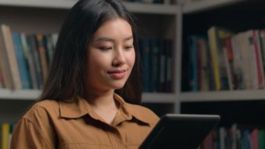 Üniversite kütüphanesinde okuyan Asyalı kız öğrenci dijital tablet kullanarak sınav hazırlama görev listesi zaman çizelgesi sınıfını kontrol ederek konsept eğitim için yeni başvuru modern teknoloji öğreniyor.