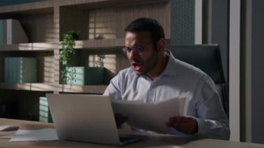 Hintli Arap asıllı Amerikalı kızgın iş adamı öfkeli öfke bunalımı yaşıyor kağıt faturaları yüzünden endişeli erkek muhasebeci yanmış evrakları dizüstü bilgisayarına bakarak at gitsin