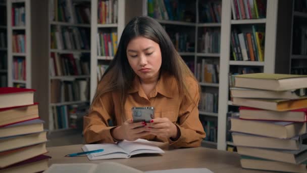 悲しみのストレス 大学図書館のアジアの女性 携帯電話で悪いニュースを読むメールをチェックする 失望した中国の女性学生 通知失敗試験 奨学金を失う — ストック動画