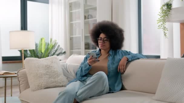 リラックスした落ち着いたアフリカ系アメリカ人女性スワイプタッチスクロール携帯電話チェックソーシャルメディア携帯電話アプリ少女自宅でオンラインEコマースアプリケーションで購入を選択 — ストック動画