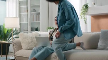 Afrika kökenli Amerikalı kadın kız arkadaş oturma odasına gel koca erkek arkadaşının yanına otur bilgisayarla birlikte internet ürünleri seçerek sohbet et bilgisayardan dizüstü bilgisayar alışverişi yap bilgisayardan bilgisayarın bilgisayarına bak.