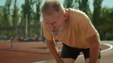 Beyaz, yorgun, yaşlı bir adam koşucu spor yapmaktan yoruldu. Sağlıklı yaşam tarzı stadyumu dışında egzersiz antrenmanı yapıyor. Yaşlı bir erkek dinlenme zorluğu çekiyor.