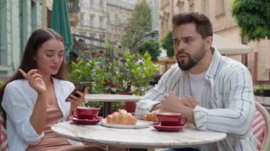 Kafede gülümseyen Avrupalı genç bir çift. Duygusal mesajlaşma, akıllı telefon, görmezden gelme. Sabit bakışlar.