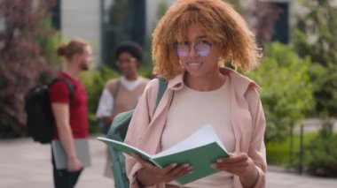 Açık havada kitap okuyan Afro-Amerikan öğrenci kız öğrenci öğrencilerin arka planlarında çeşitli ırkçı öğrencilerin arkadaşlarının jestleri gibi davranışlar sergilemesini öneriyor.