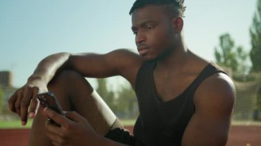 Afrika kökenli Amerikalı erkek sporcu akıllı telefon sporu ve teknolojisi ile şehir erkeğinin spor salonundaki spor salonunda spor yaparken cep telefonunu kullanması ve dışarıda antreman sonrası cep telefonu kullanması.