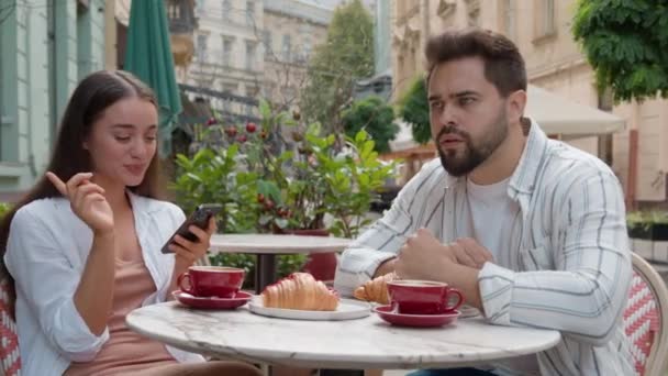 城市咖啡店里的一对欧洲年轻夫妇笑着 发短信 智慧电话 忽视男人凝视 凝视远方 沮丧的关系 户外早餐 上网成瘾 — 图库视频影像