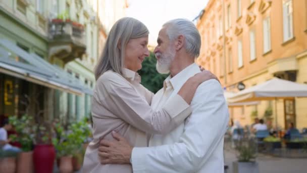 ドリーミーシニアコーカサス成人成熟した灰色髪のカップルの女性男性は 外で良い未来を考えるカドルを抱擁する笑顔のカメラを見ています メディカルヘルスケア退職結婚休暇旅行 — ストック動画