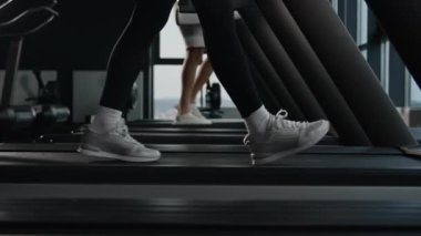 Sporcular spor ayakkabılı iki koşucu kadın ve erkek kaslı bacaklar koşu bandında koşuyor spor salonunda spor ayakkabıları giyiyor koşu makinesinde adım adım yürümek için spor ayakkabıları giyiyor.