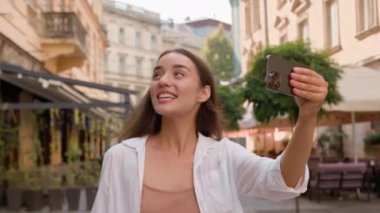 Kafkasyalı neşeli kadın şehir merkezinde geziyor görüntülü konuşma yapıyor sohbet ediyor akıllı telefon görüşmeleri turizmi kameraya bakıyor gülümseyen kız tatillerine gidiyor