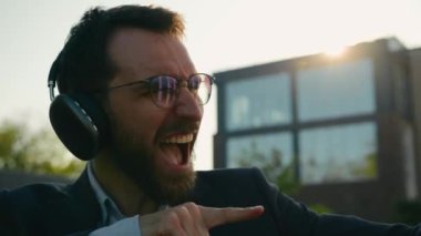 Kafkasyalı mutlu iş adamı komik neşeli iş adamı kulaklıklı kaygısız erkek kulaklıkla müzik dinliyor enerjik ses şarkıları dinliyor güneş ışığında dans ederek hafta sonu şehirde eğlenin.