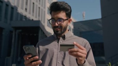 Arap Hintli iş adamı banka kredi kartı ödemelerini açık havada cep telefonuyla yapıyor. Müşteri güvenlik kodu girerek şehirde hizmet ödemesi parası transferi için ödeme yapıyor.