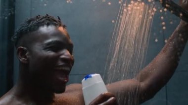 Mutlu Afro-Amerikalı adam banyoda şarkı söylüyor çıplak erkek duş jeli şampuanıyla şarkı söylüyor vücut bakımını yıkıyor temizlik yapıyor müzik dinliyor, sabah banyoda enerji banyosu yapıyor.