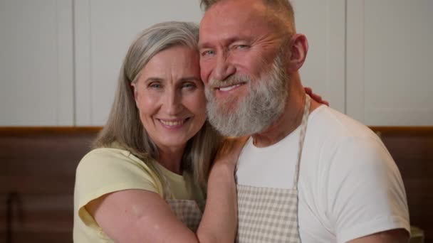 快乐的家庭白种人退休夫妇成熟的中年白头发女人在家里做饭厨房里拥抱拥抱温柔的爱情关系成熟的老夫妇微笑保险贷款抵押贷款 — 图库视频影像