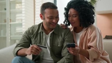 Evli çift, Afrikalı Amerikalı kız arkadaş ve erkek arkadaş mutlu erkek kadın kredi kartı ile bilet alıyor cep telefonu kullanıyor teslimat internet bankacılık hizmeti evde kolay para ödemesi