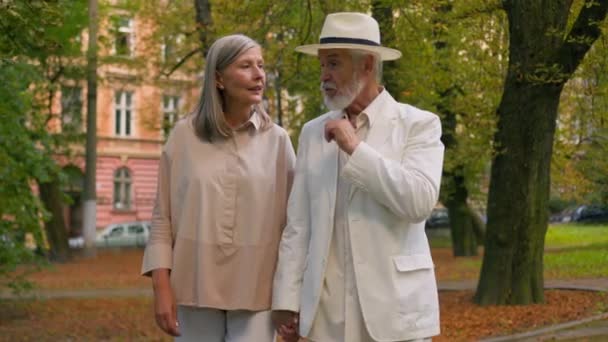 快乐而又优雅的白种人夫妇家庭中老女人牵着手谈论着一起走出城市公园的事 积极的退休 暑期放松自然快乐 — 图库视频影像