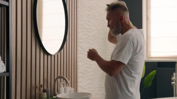 一位英俊的白种人自信满满的男人在浴室里看着镜子里倒影 用刷子梳理胡子梳头 年长的成熟男性用刷子梳理灰白的头发 为早上的退休人员做好准备 — 图库视频影像
