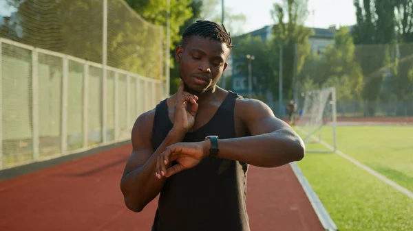 African American man runner jogger athlete muscular sportsman training outdoors athletic ethnic guy using smart band checking neck pulse heart rate result on smartwatch before running on sport stadium