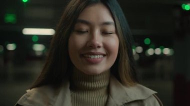 Asya portresi etnik kızı gülümseyen Çinli kadın mutlu güzel bayan Japon kadın karanlık araba otoparkında poz veriyor güzel Asyalı iş kadını dişlek gülüşü ile güzel iş kadını.