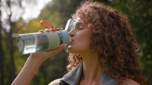 スポーティな運動疲れた喉の渇いたコーカサス女性ランナーのジョギングガールスポーツ女性は 屋外でトレーニングを実施した後 フィットネスボトルの健康的なライフスタイルでリフレッシュ飲料を飲む — ストック動画
