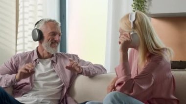 Neşeli yaşlı, yaşlı, Kafkasyalı, evli, büyükanne ve büyükbaba, müzik dinleyen, kulaklık takan, dans eden, eğlenen, kaygısız büyükanne, büyükbaba, hafta sonunun keyfini çıkaran, evde kanepede oturan kadın.