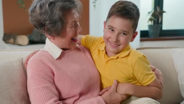 愛するコーカサスのおばあさんのおばあちゃんの女性楽しい週末を過ごす 居心地の良いソファーで家で孫の少年子供と一緒に笑顔の幸せな家族2世代を演奏 笑い声をあげるトリック — ストック動画