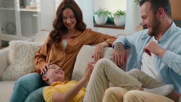 愛する両親は家でソファーで息子と遊ぶ ケアフリー 母親のティックル 楽しむ ゲーム カドリング 一緒に過ごす 幸せなコーカサス家族 — ストック動画