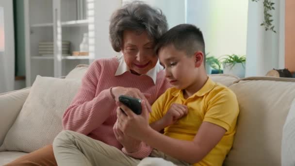 爱白种人孙子男孩儿教老年妇女外婆用智能手机在网上商店浏览社交媒体两代家庭一起呆在家里 — 图库视频影像
