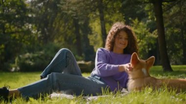Açık havada dinlenen genç kadın evcil hayvan sahibi sevimli yavru köpeği okşayan mutlu genç kız Galli Corgi köpeği ile oynayan sadık evcil hayvan köpekçik aşk hayvanı şehir parkında çimenlerde birlikte eğleniyor.