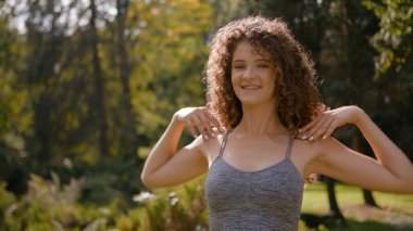 Sağlıklı sporcu kadın döner el çemberi. Omuzlarıyla dairesel hareketler yapar. Açık havada spor yapan beyaz kadın sporcu.